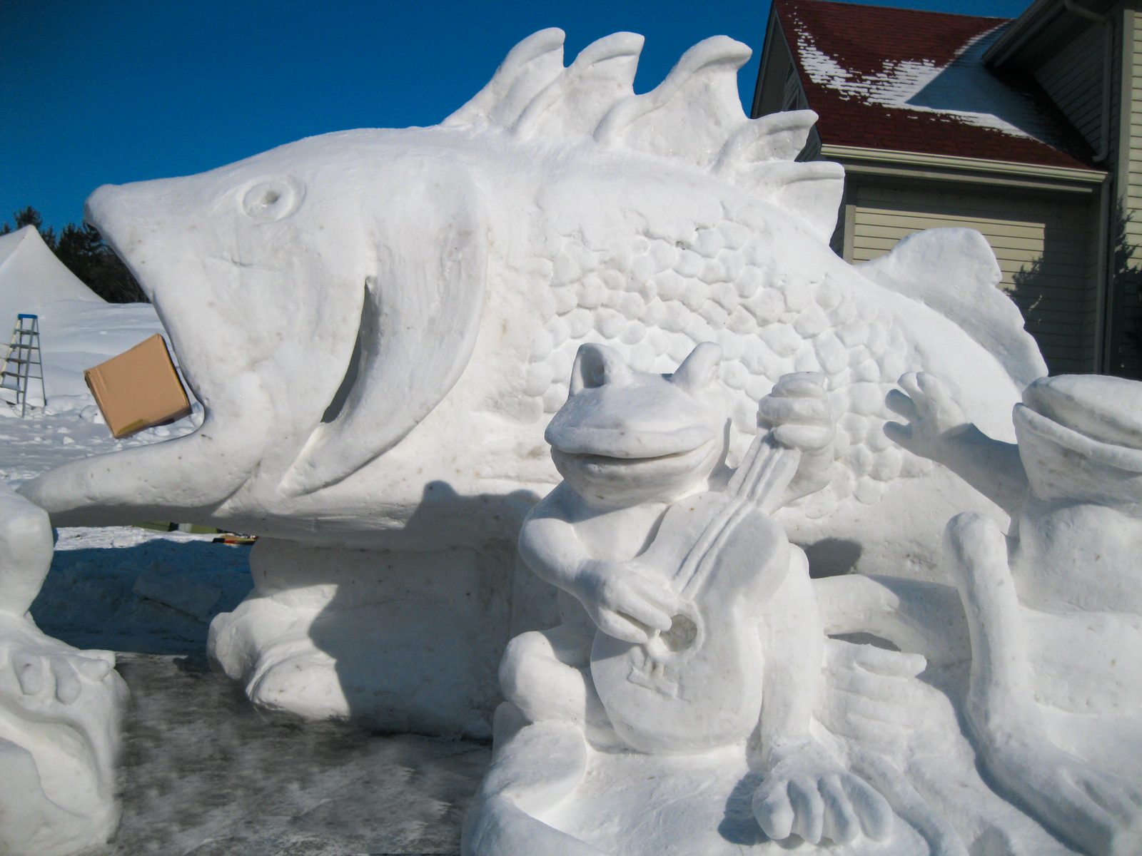 Detailed snow sculpture of a frog playing guitar alongside a giant fish in Frankenmuth, Michigan.